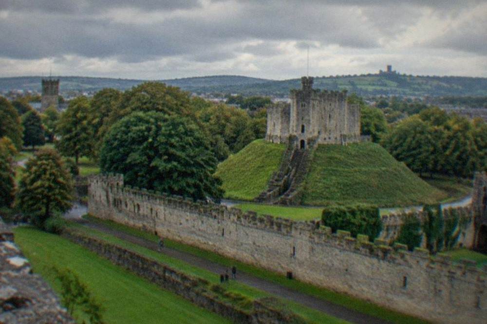 Rolling green hills with dry stone walls and a distant castle tower under a cloudy sky