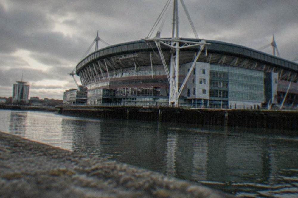 A large rugby stadium with a closed roof and rows of empty seats under floodlights