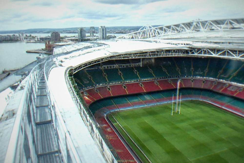 A view from a stadium roof walk looking down at a green pitch and seating tiers