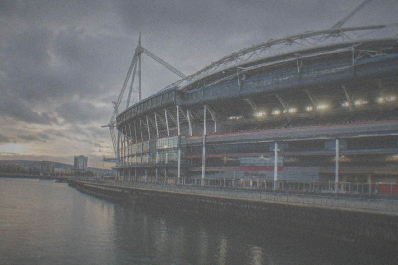 A large rugby stadium with a closed roof and rows of empty seats under floodlights