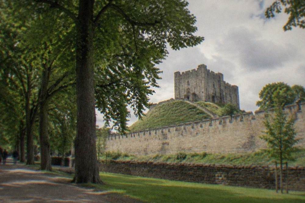 A tree-lined path through Bute Park with Cardiff Castle walls rising behind the trees