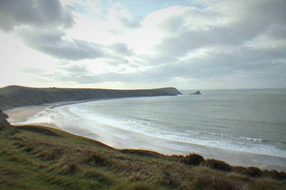 Rhossili Bay beach curving below grassy cliffs under an open sky
