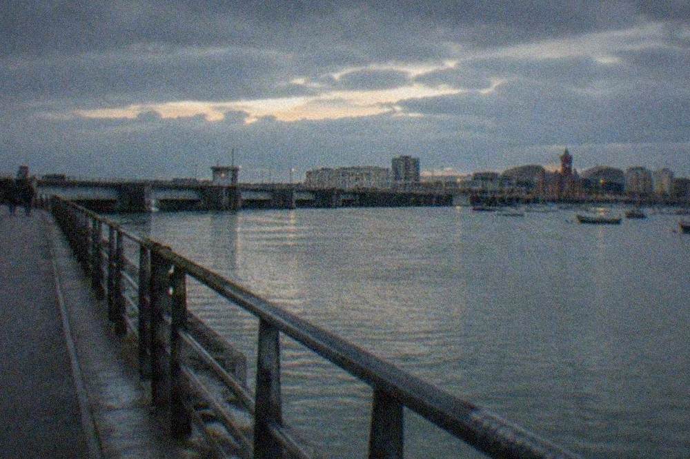 A modern waterfront walkway beside a wide bay with boats moored in the distance