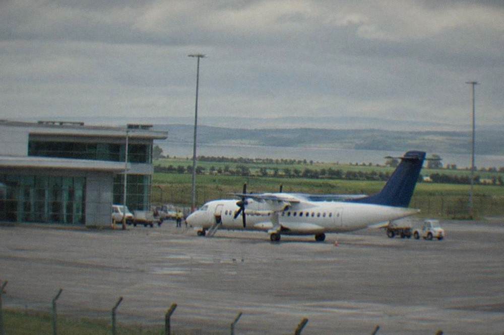 A small regional airport terminal building under an overcast sky with a parked aircraft outside