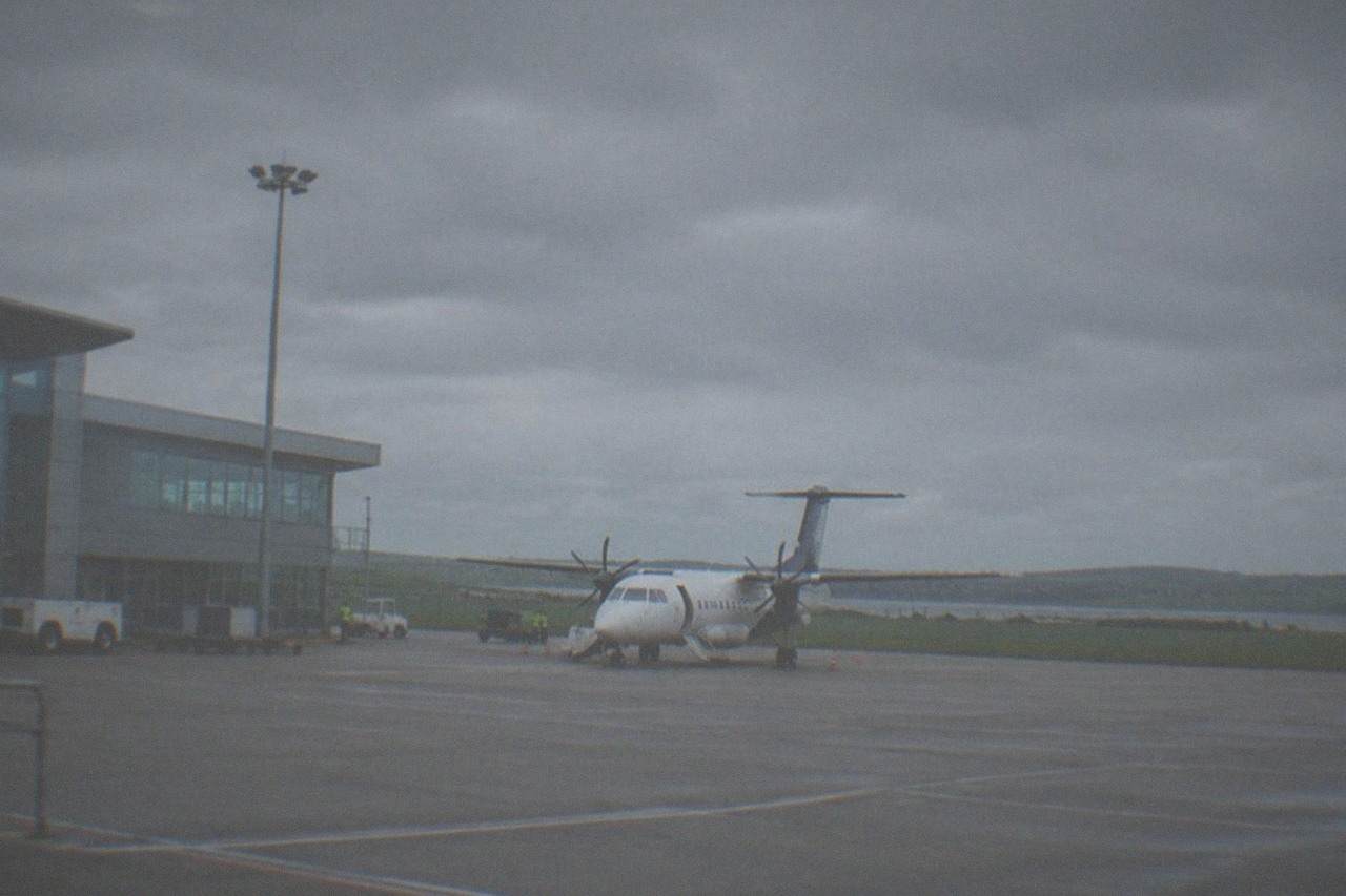 A small regional airport terminal building under an overcast sky with a parked aircraft outside