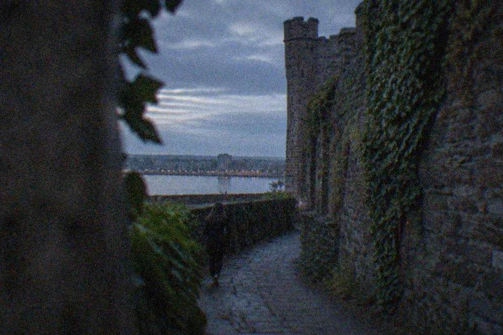 A narrow stone alley beside a castle wall in Cardiff with ivy growing along the edges