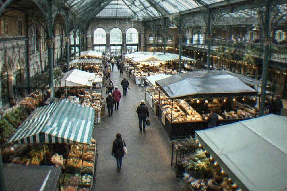 A Victorian market interior with a glass roof and food stalls beneath it