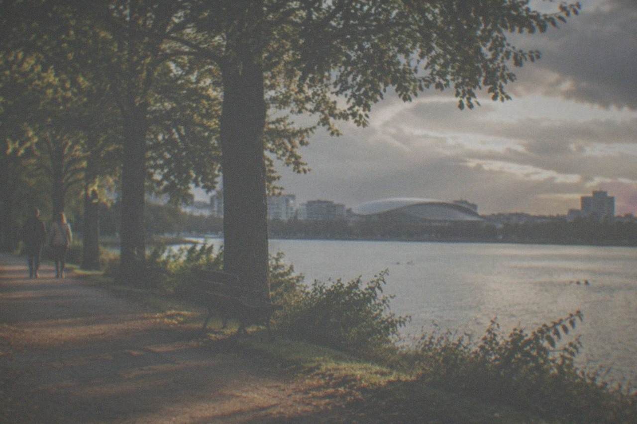 A quiet tree-lined path beside a Victorian park lake in Cardiff at golden hour
