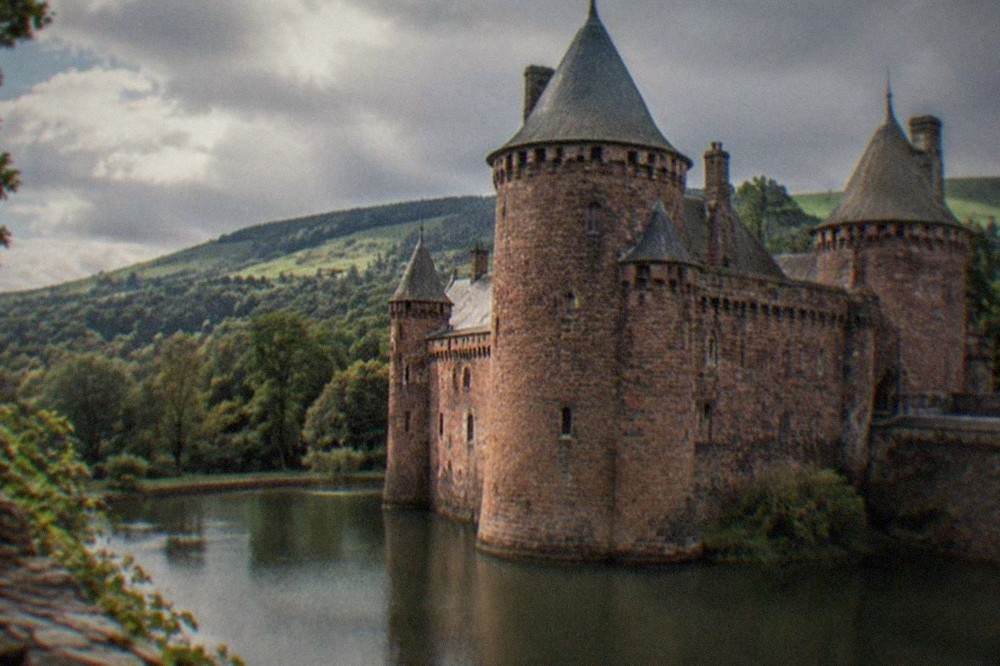 Stone castle towers rising above a wide moat with green hills behind