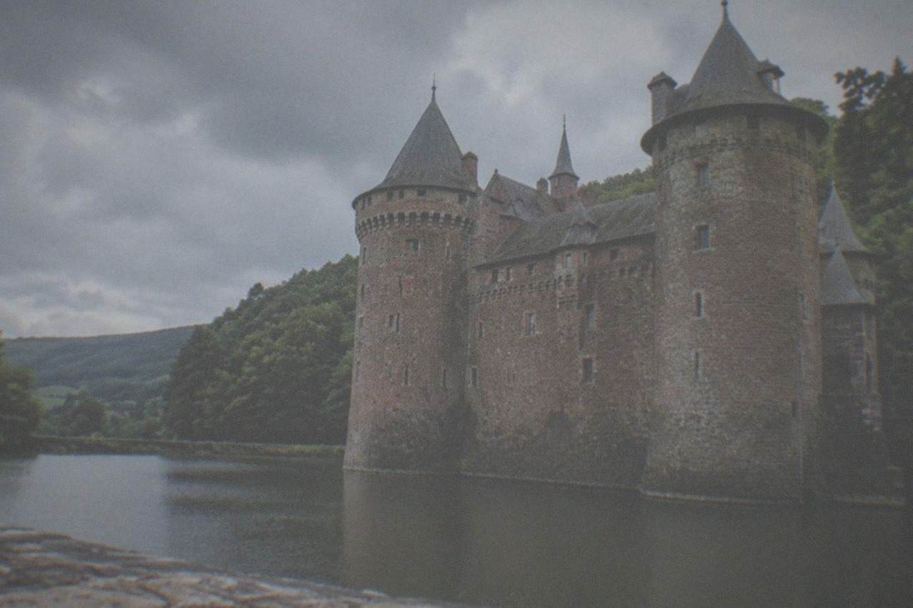 Stone castle towers rising above a wide moat with green hills behind