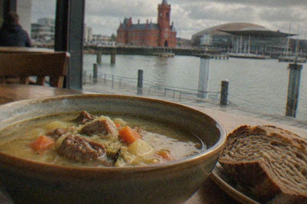 A traditional bowl of cawl soup with bread on a wooden table in a Cardiff restaurant