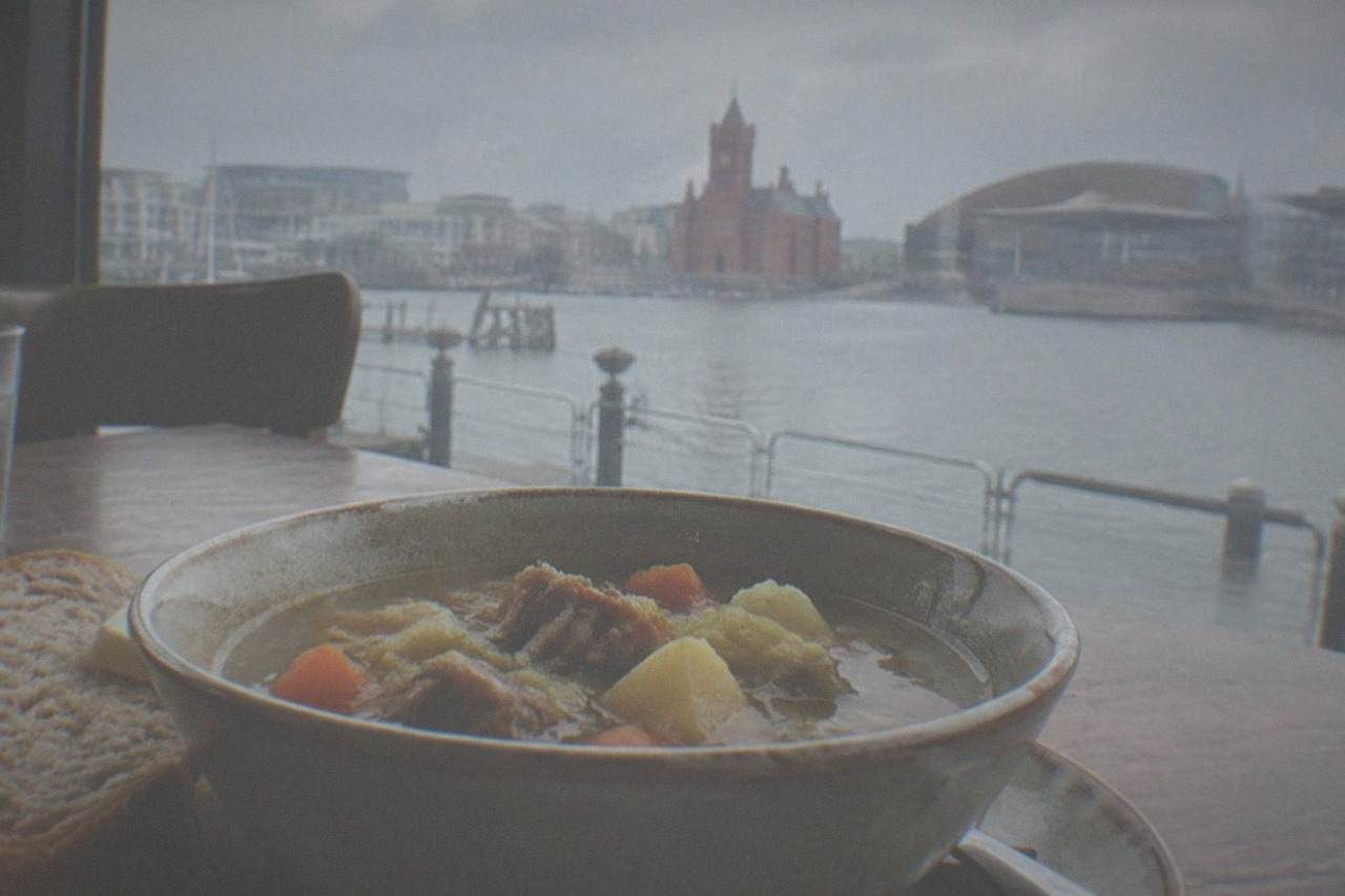 A traditional bowl of cawl soup with bread on a wooden table in a Cardiff restaurant
