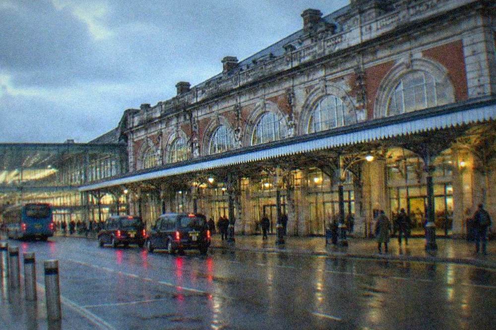 A modern glass railway station concourse with departure boards and passengers