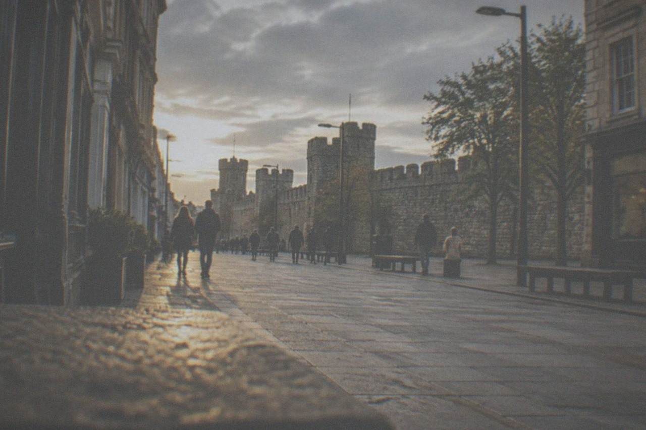 A wide pedestrian street in central Cardiff with shopfronts and a castle wall in the distance