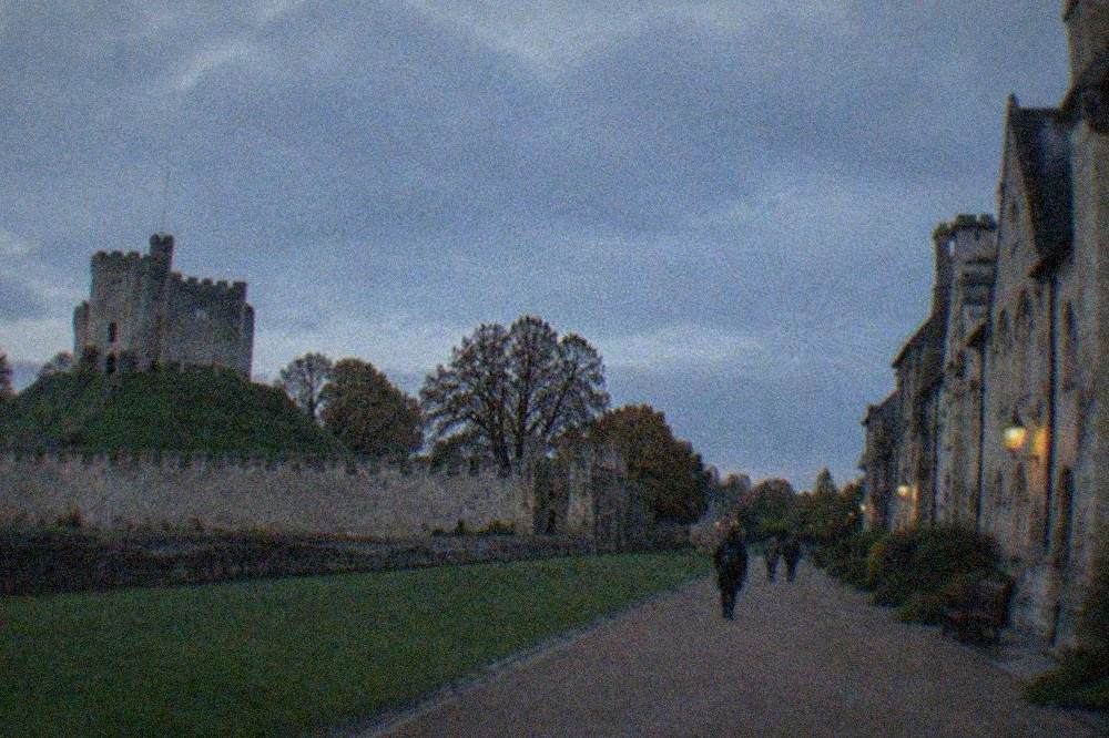 A row of historic stone buildings arranged along a wide open-air museum path under a pale sky