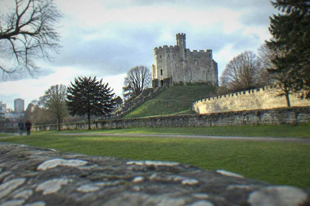 A stone castle keep rising above parkland trees on the edge of a city centre