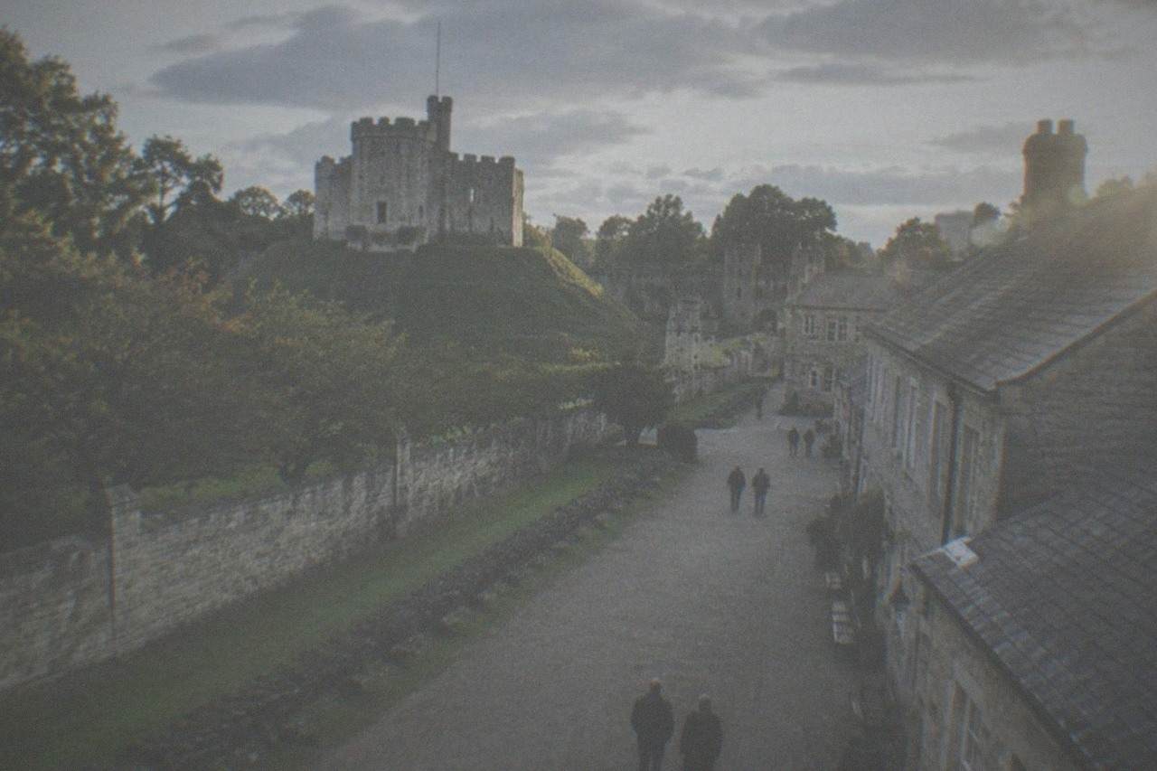 A row of historic stone buildings arranged along a wide open-air museum path under a pale sky