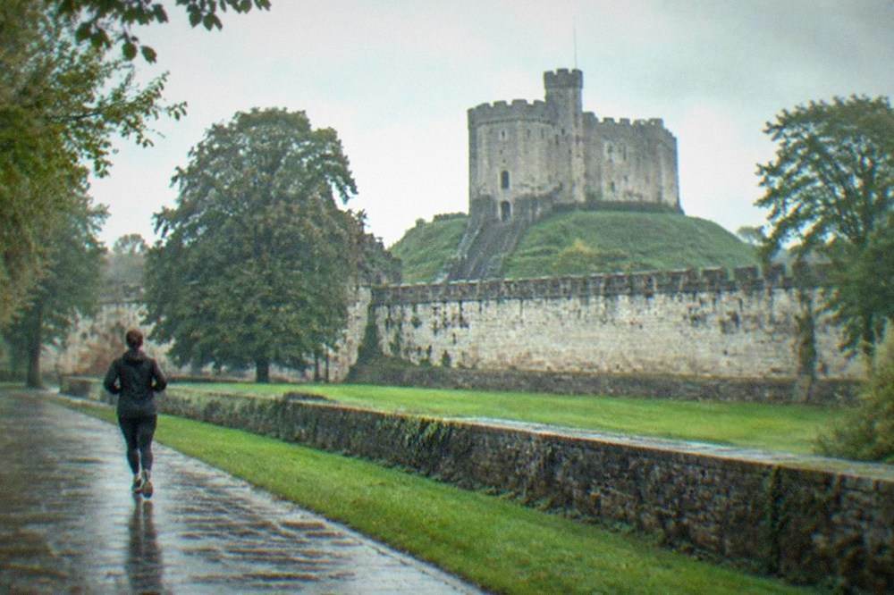 A stone castle keep rising above city parkland with trees in the foreground