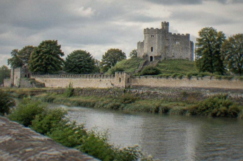 A stone castle keep rising above a green river valley in South Wales
