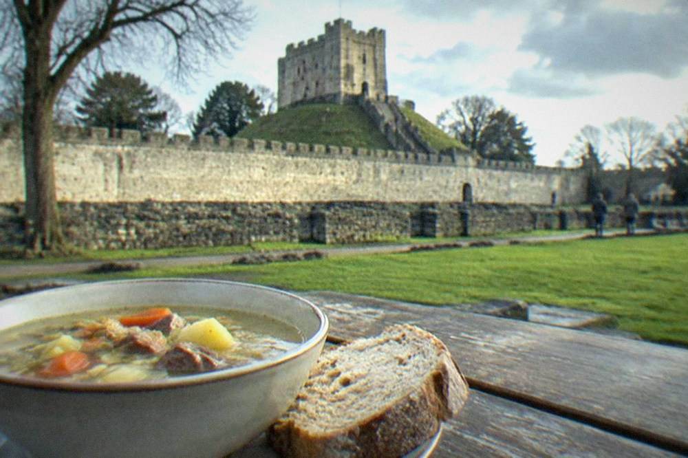 A bowl of traditional Welsh cawl soup with bread on a wooden table
