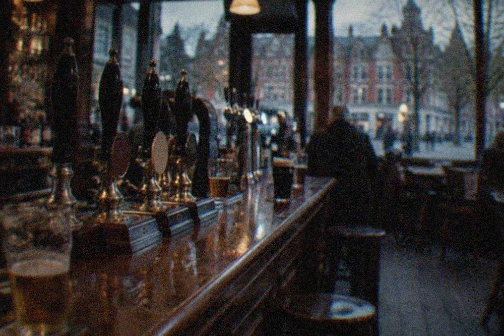A dimly lit traditional pub interior with a long wooden bar counter and rows of beer pumps