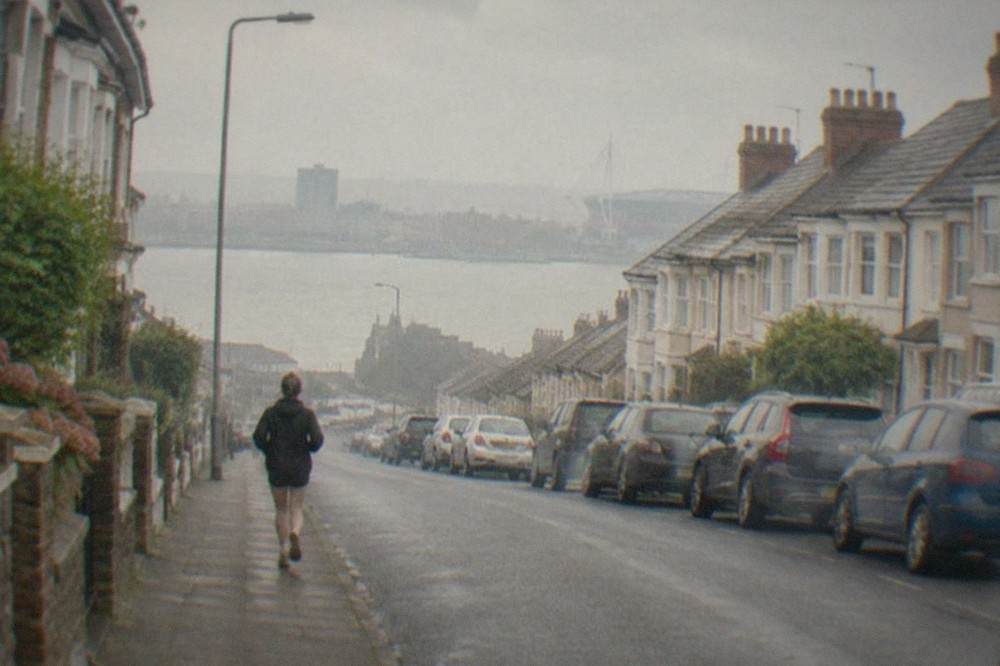 A quiet residential street in Cardiff with terraced houses and parked cars