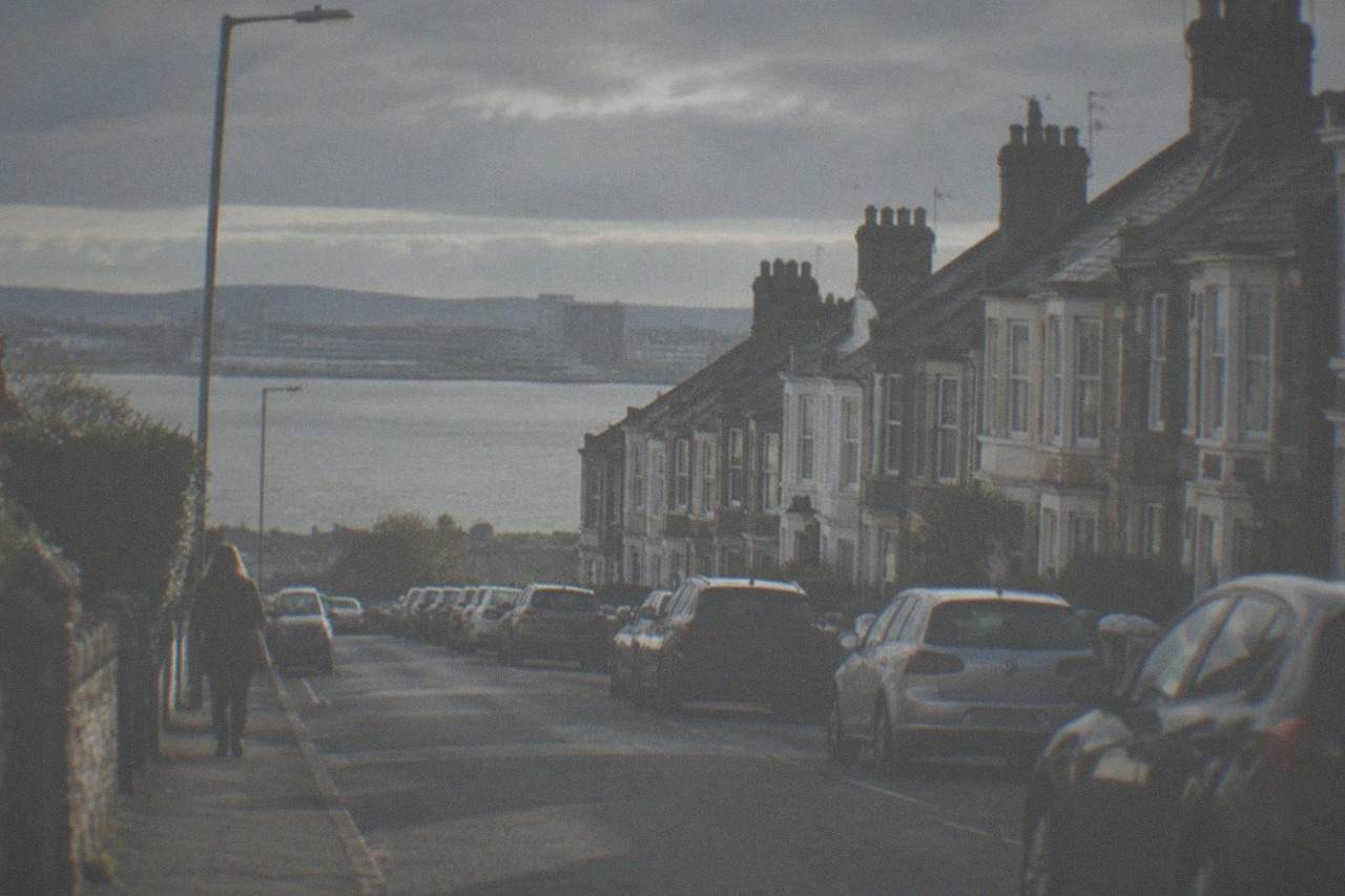 A quiet residential street in Cardiff with terraced houses and parked cars