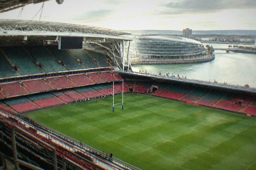 A wide sports stadium pitch and tiered seating seen from high on the stand structure