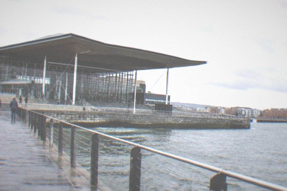 Cardiff Bay waterfront promenade on a grey day with the Senedd building and choppy harbour water