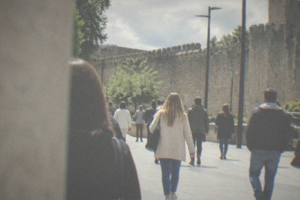 Shoppers walking along a pedestrianised city street with a castle wall beyond