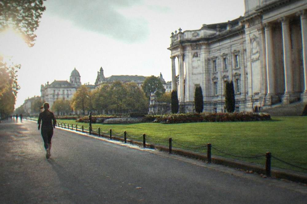 The stone facade and columns of a civic building beside lawns and flowerbeds