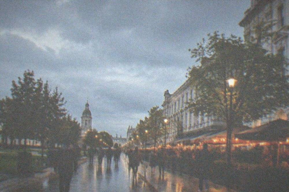 A busy evening street with lit restaurant fronts and people walking past