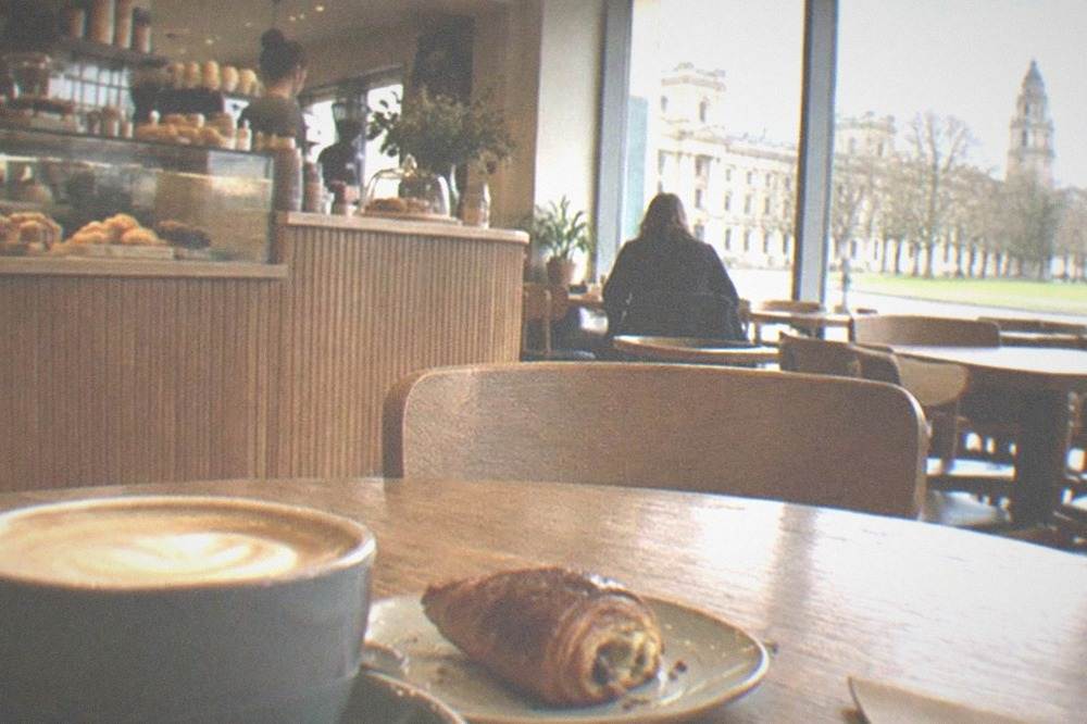 A café interior with wooden tables and a counter of pastries and coffee machines