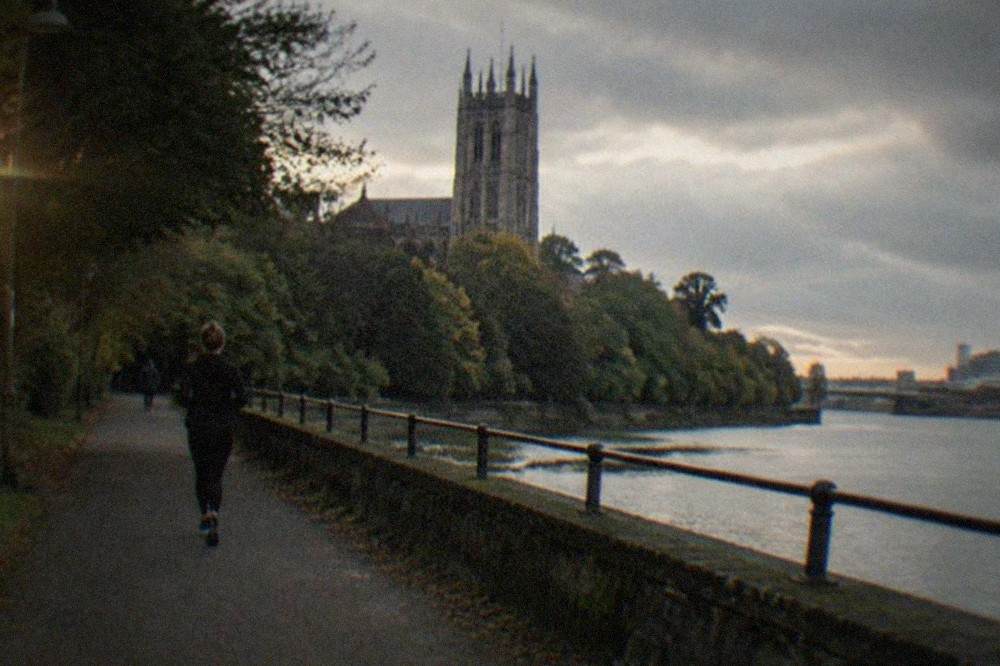 A stone cathedral tower rising above trees beside a river path