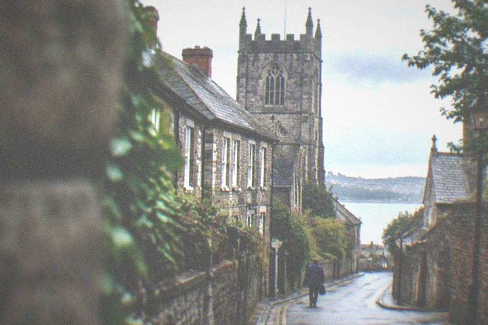 A quiet village street of stone and brick buildings leading toward a church tower