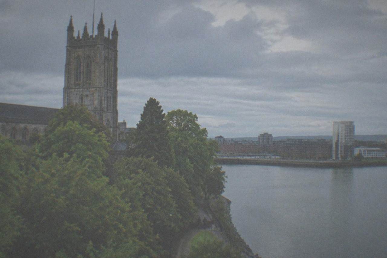 A stone cathedral tower rising above trees beside a river path