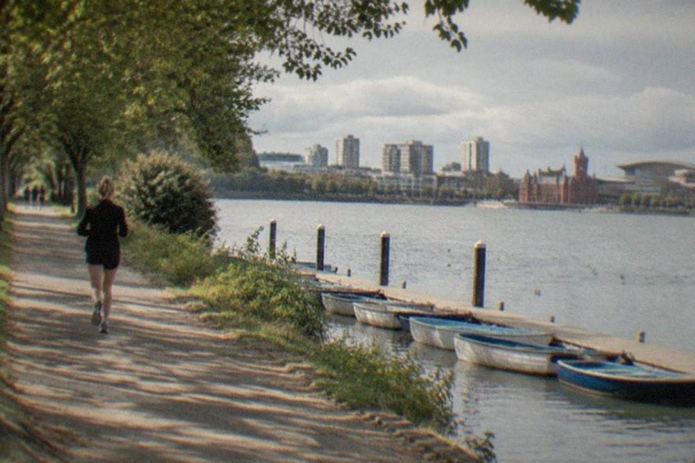 A tree-lined path beside a park lake with rowing boats moored at a wooden jetty