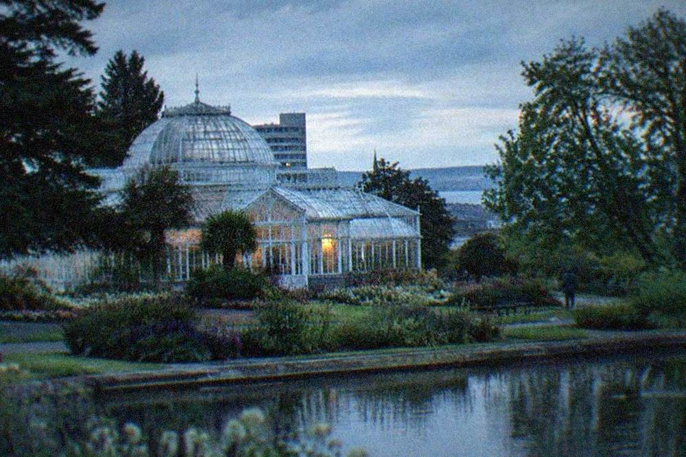 A Victorian park conservatory surrounded by flower beds and mature trees