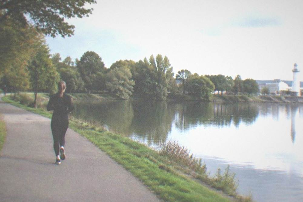 A park lake at late afternoon with trees reflected in still water and a distant lighthouse tower