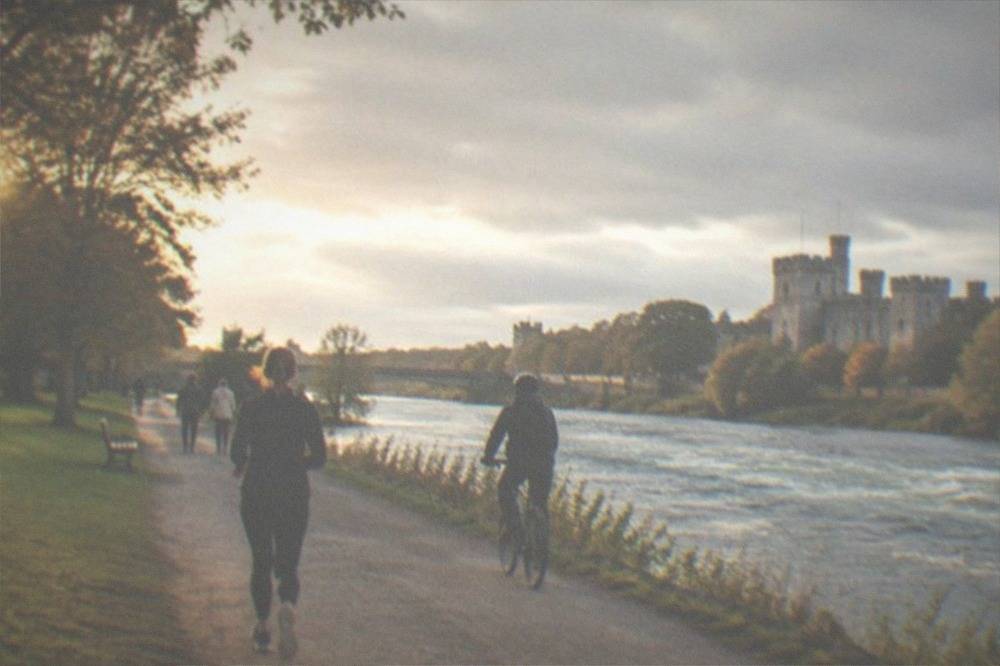 Cyclists and walkers on a riverside path beside a fast-flowing river