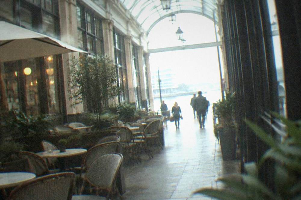 A narrow arcade walkway with a curved glass ceiling and a café with tables in the passage