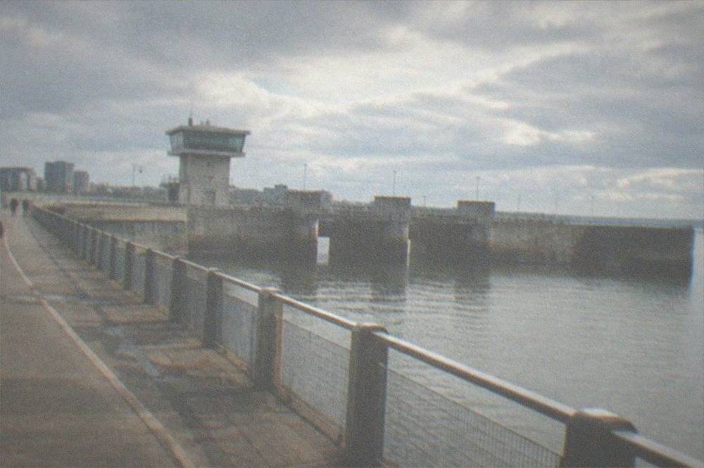Concrete lock gates and a control tower beside a waterfront path