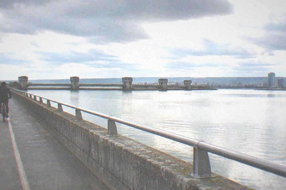 A cyclist on a flat waterfront path with calm water on one side