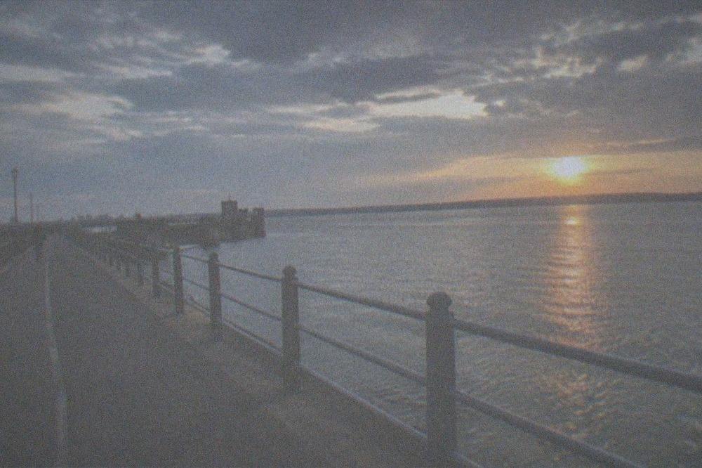 A sunset over open water seen from a waterfront path with railings