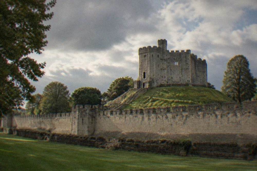 Stone keep of Cardiff Castle rising above green lawns under a partly cloudy sky