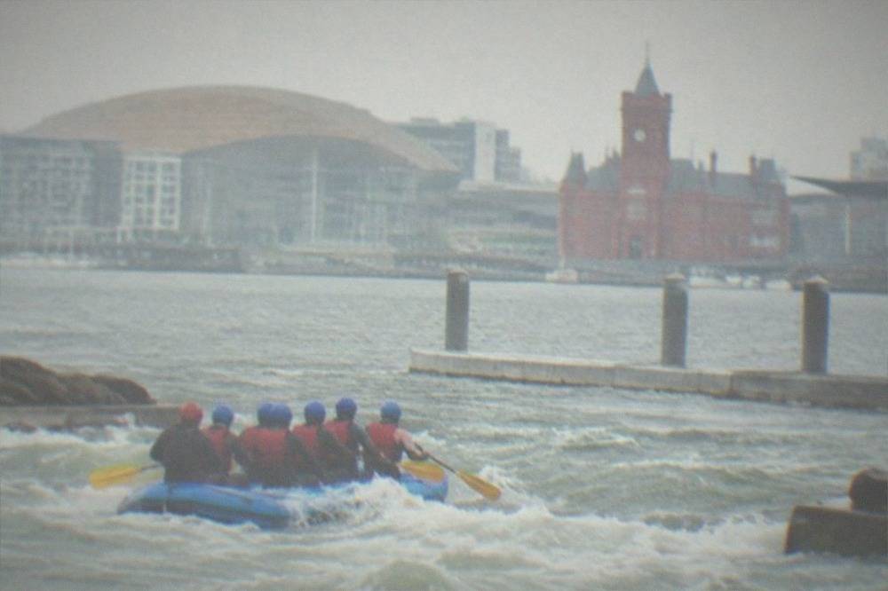 A group in helmets and buoyancy aids paddling an inflatable raft through a rapid