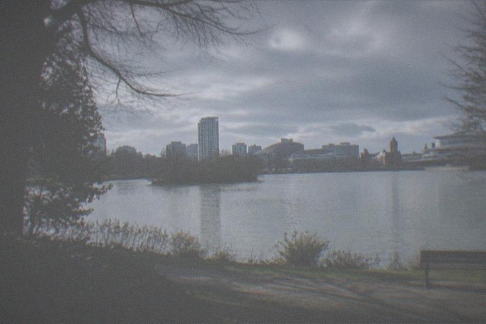 A calm lake and parkland in Cardiff with trees and a distant city skyline