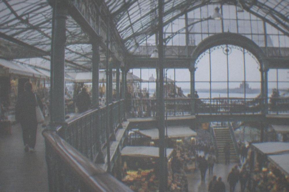 A covered Victorian shopping arcade with small independent shopfronts under a glazed roof