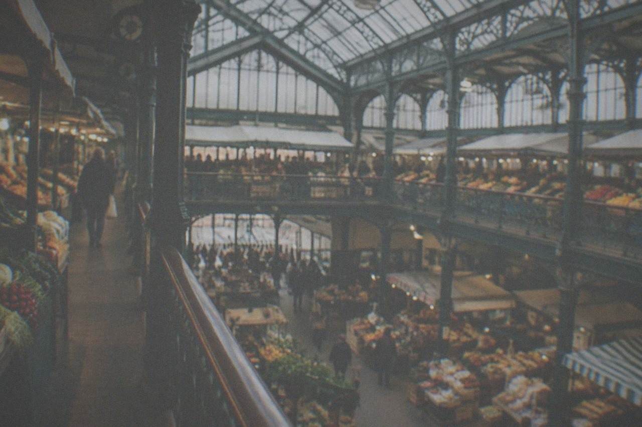 A Victorian market hall interior with a glass roof, iron columns and stalls lined with produce