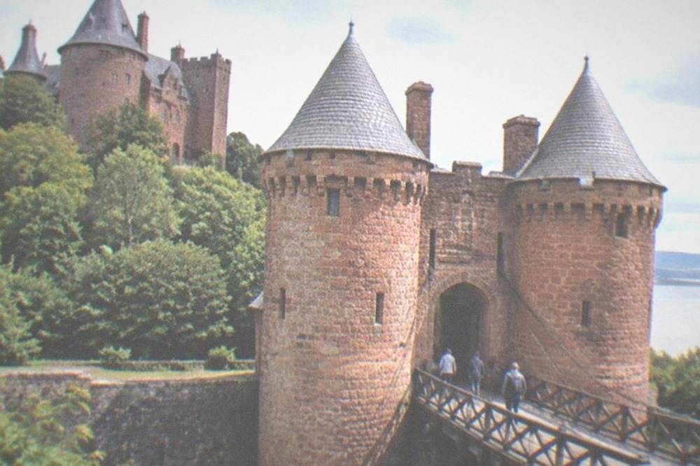 A red sandstone castle gateway with a raised drawbridge spanning a dry moat